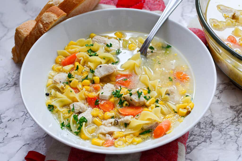 A bowl of chicken noodle soup with corn and carrots.