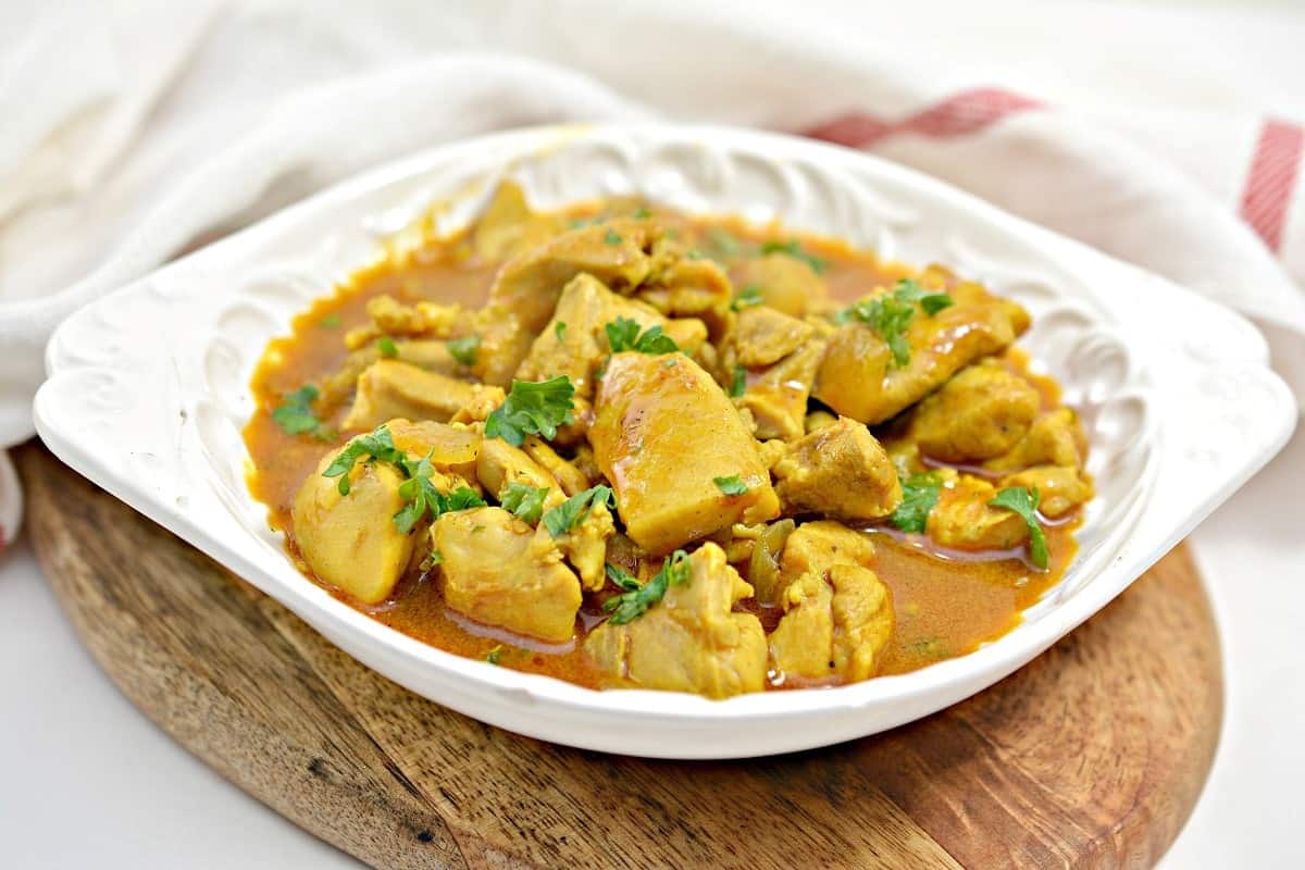 Chicken curry in a white bowl on a wooden cutting board.