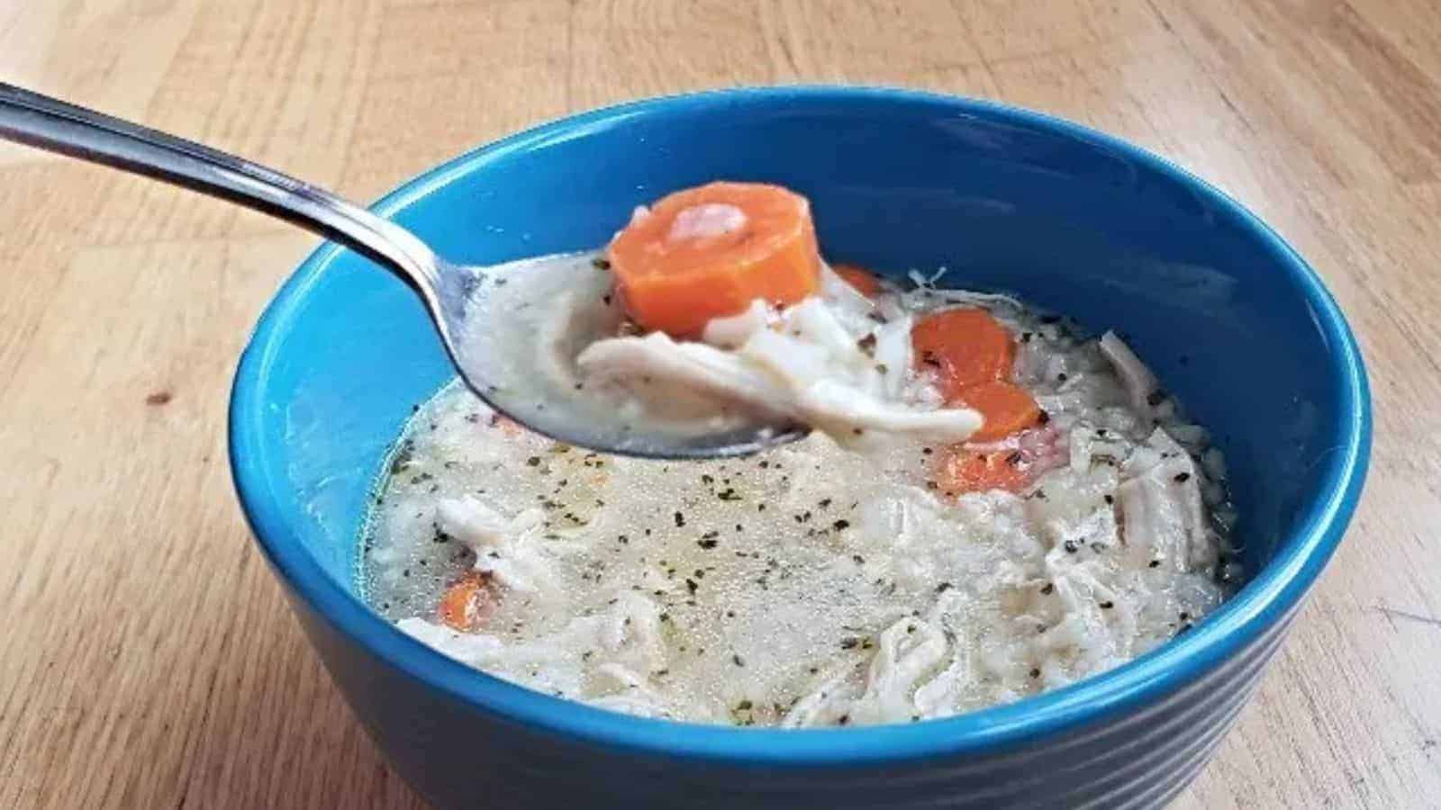 Image shows Chicken and rice soup on a spoon with the full blue bowl behind it.