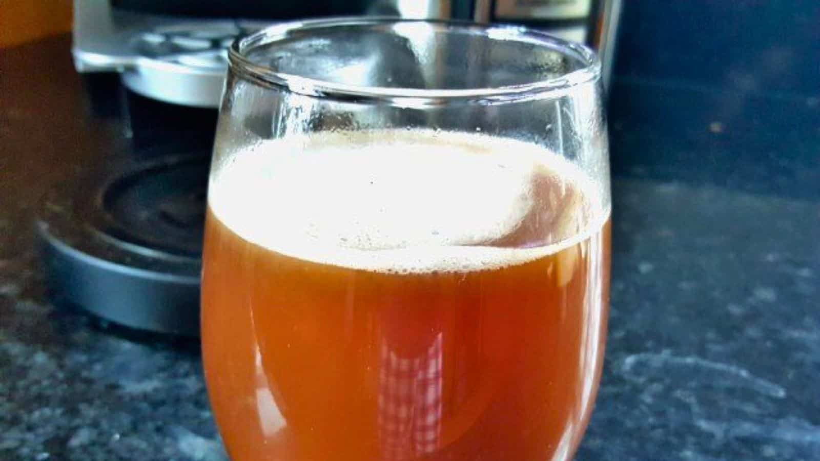 Image shows a glass of chocolate cherry latte in front of a coffee maker.