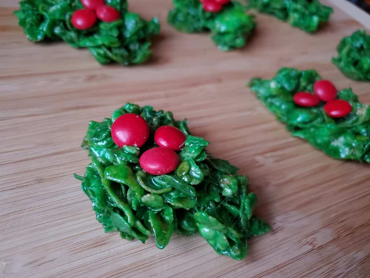 Image shows classic holly wreath cookies on a wooden board.