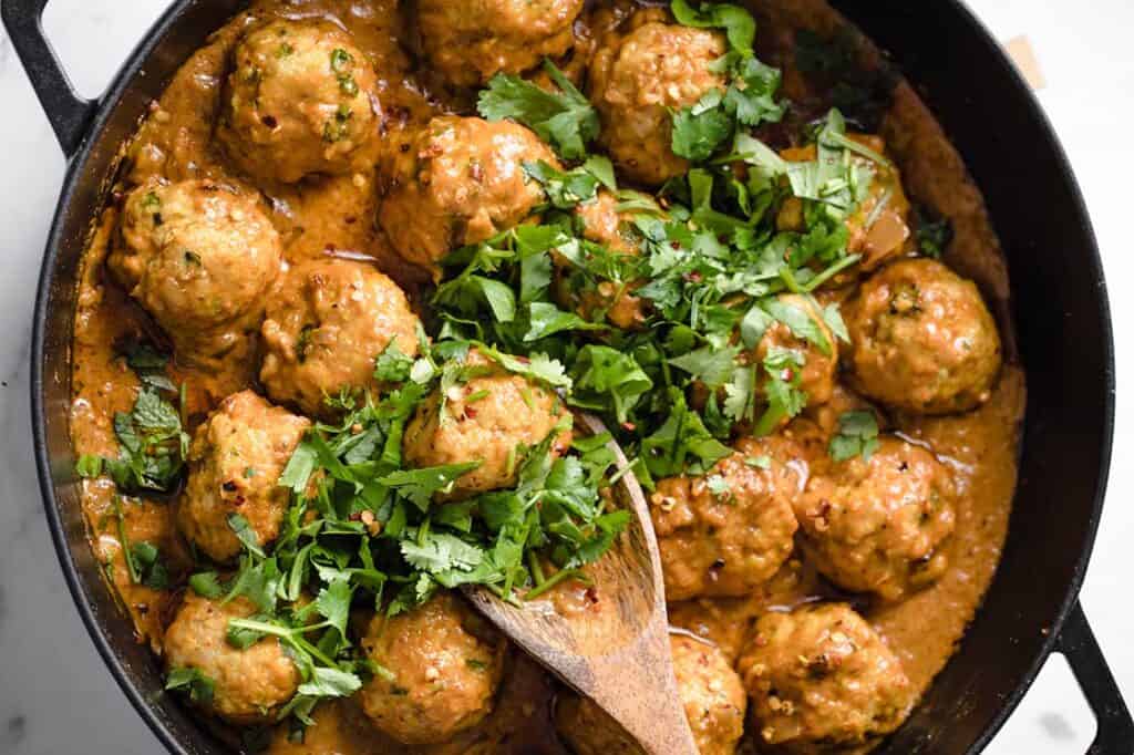 Thai meatballs in a skillet with a wooden spoon.