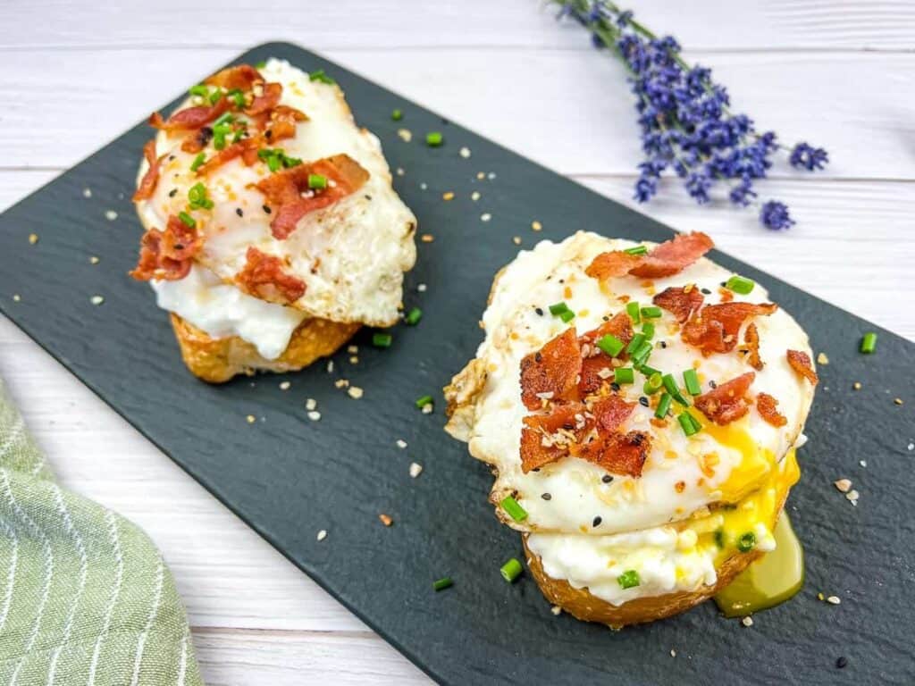 Two cottage cheese toast with bacon & poached egg on a slate plate.