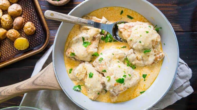 Chicken breasts in a sauce with potatoes and parsley on a wooden table.