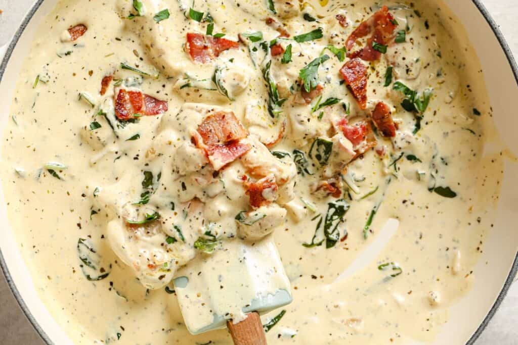 A pan filled with a creamy sauce with chicken, bacon, and spinach.