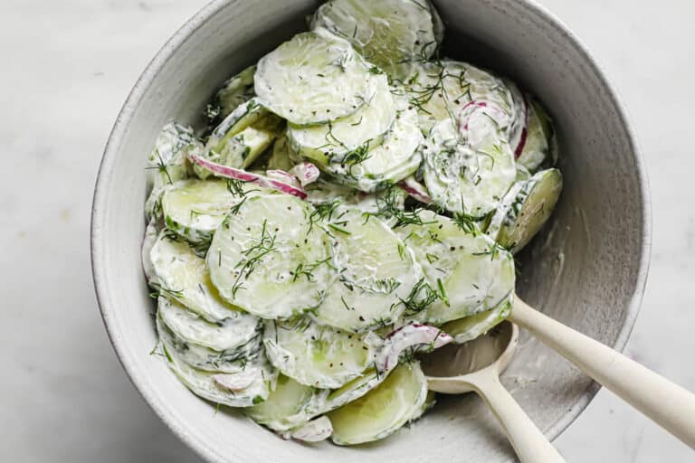 Cucumber salad in a bowl with a wooden spoon.