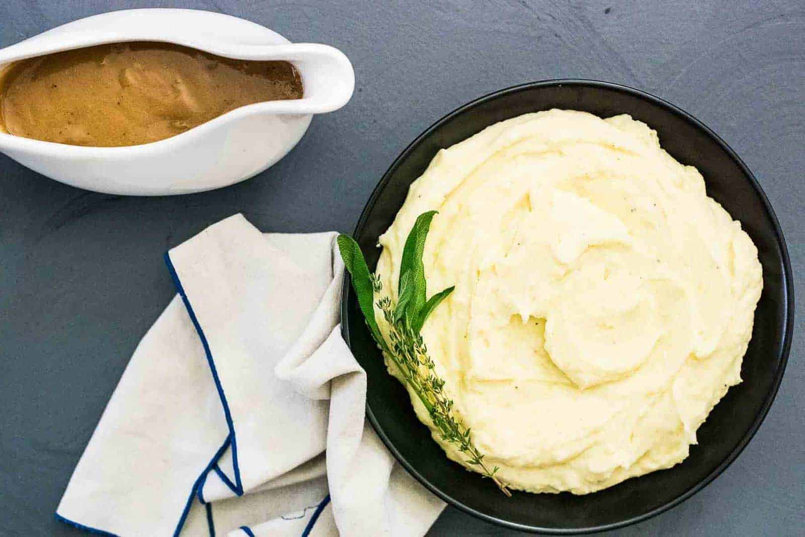 A bowl of mashed potatoes with gravy and sprigs of thyme and sage.