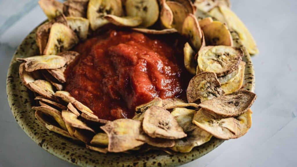 A bowl filled with banana chips and tomato sauce.