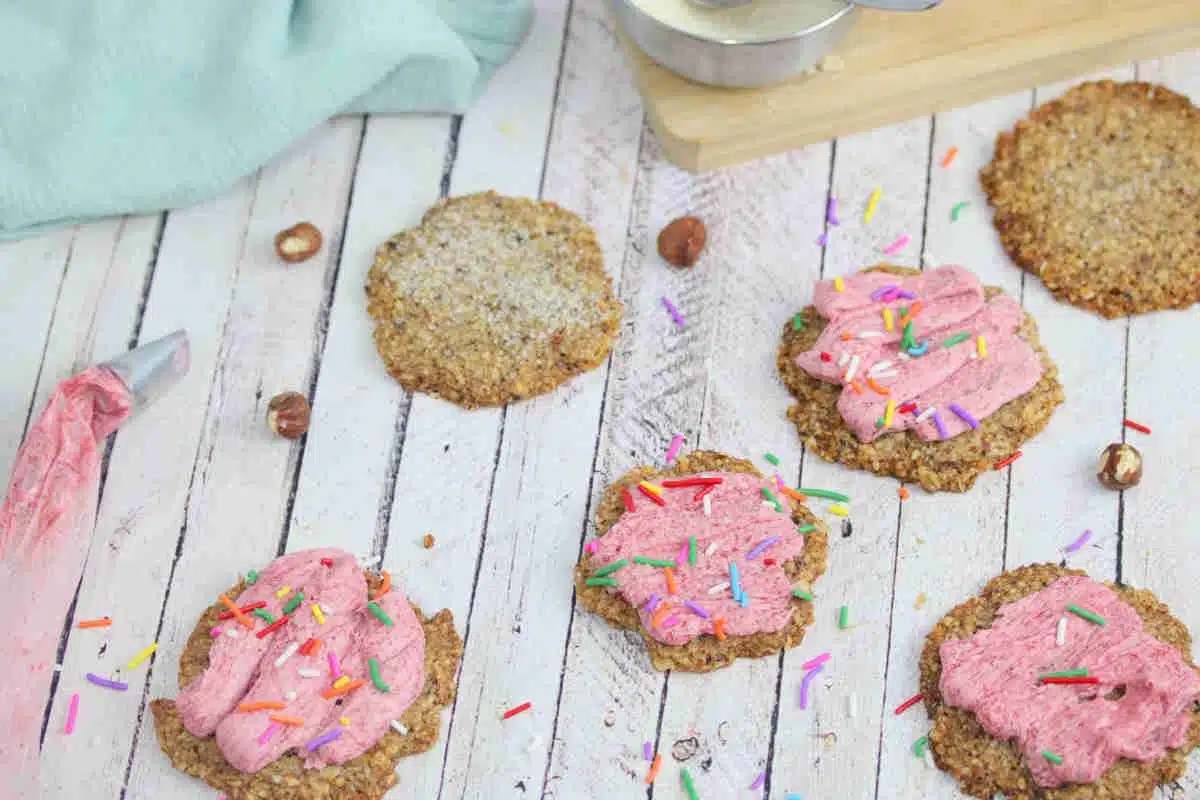 Sugar cookies with pink icing and sprinkles, a blue linen and bowl of sugar behind them.