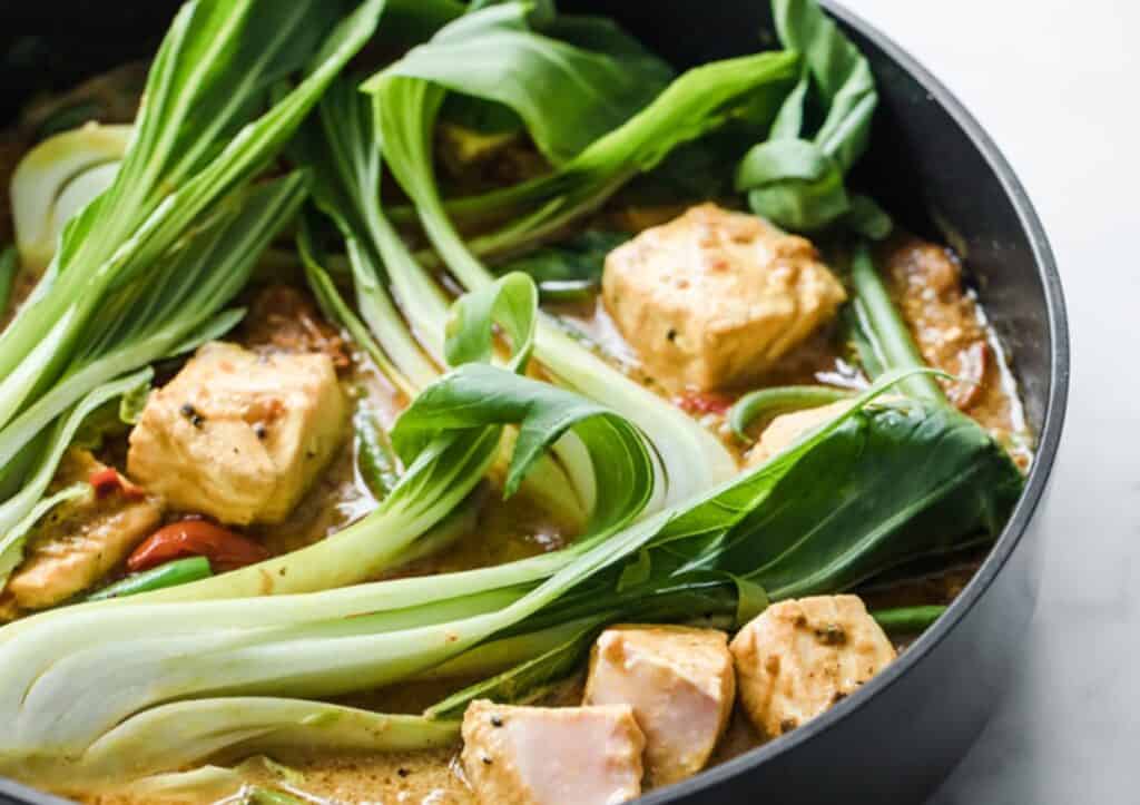 A pan with curry salmon and bok choy in a sauce.