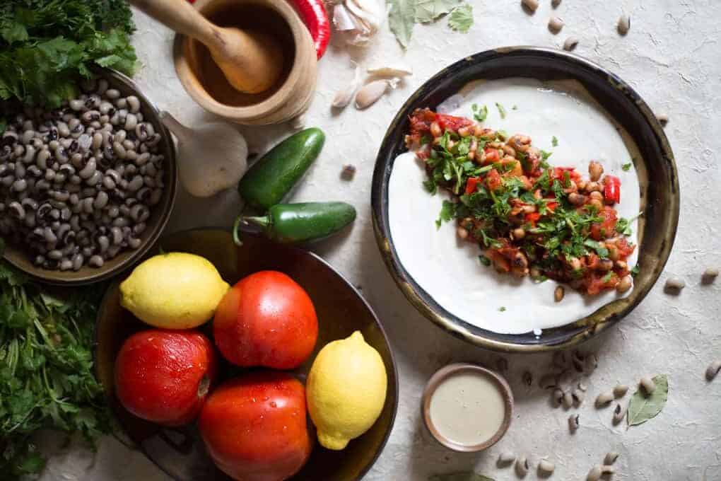 A mouthwatering bowl of hummus adorned with vibrant tomatoes, savory olives, and fragrant herbs. Perfect for holiday appetizers!