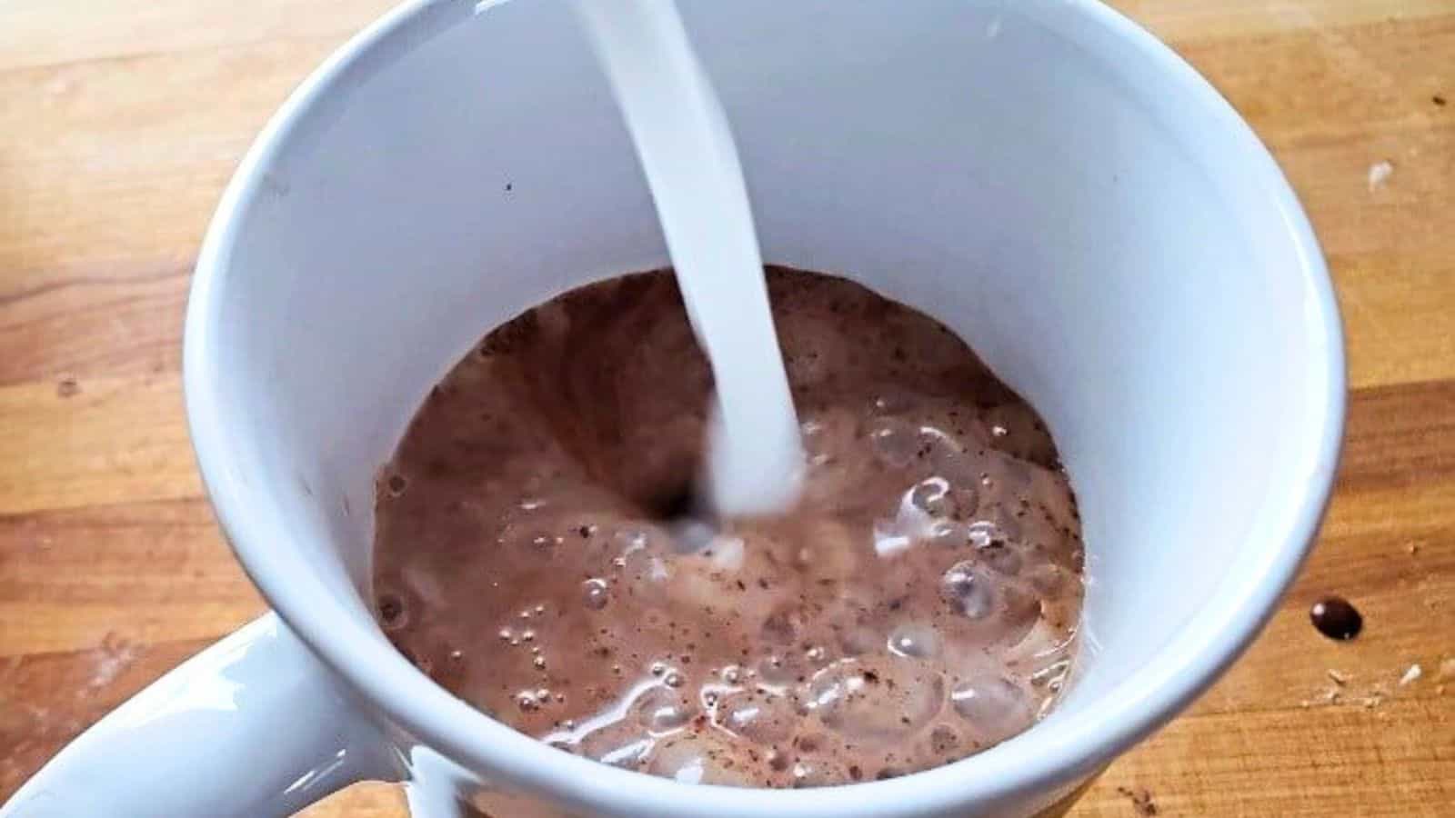 Image shows hot milk being poured into a mug with chocolat chaud base.