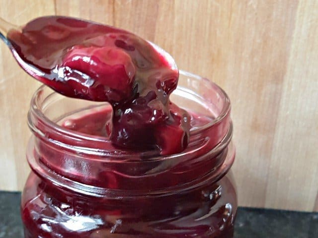 Image shows cherry syrup dripping off a spoon into the jar.