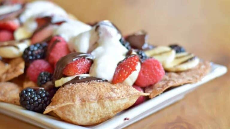 Image shows dessert nachos on a plate topped with fruit and whipped cream.