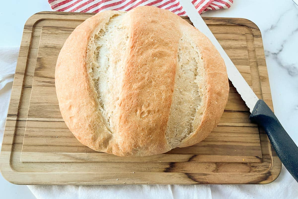 A loaf of peasant bread on a cutting baord with a knife with it.