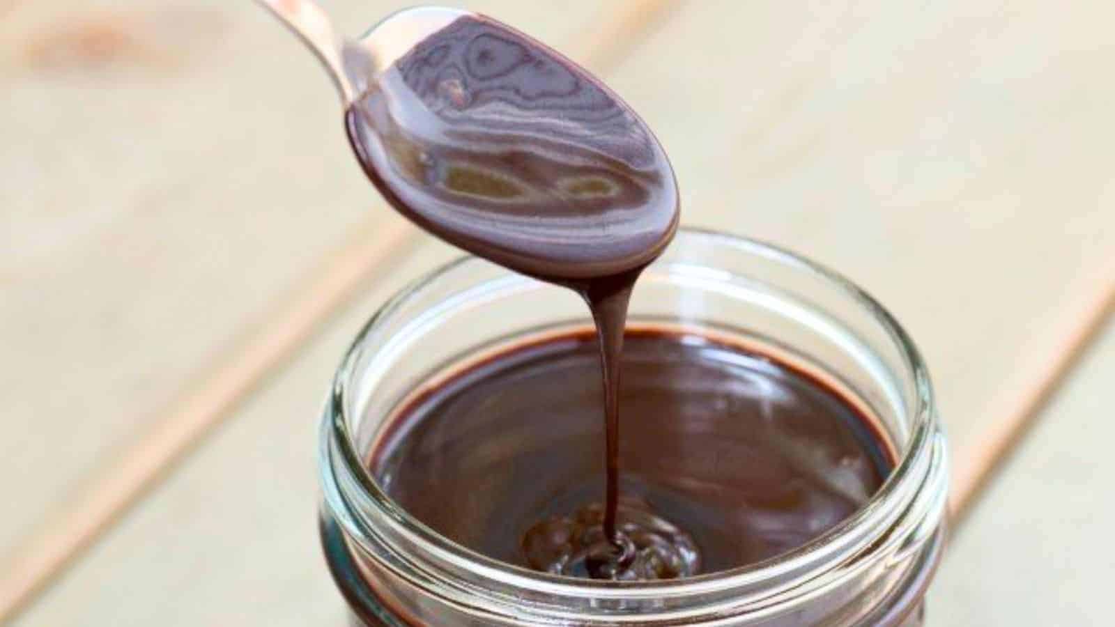 Image shows a spoon drizzling homemade espresso hot fudge sauce back into its jar.