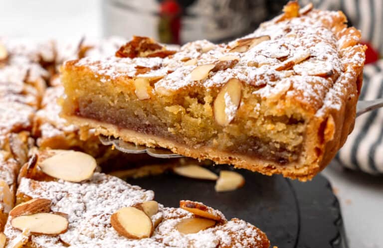 A slice of bakewell tart with powdered sugar and almonds.