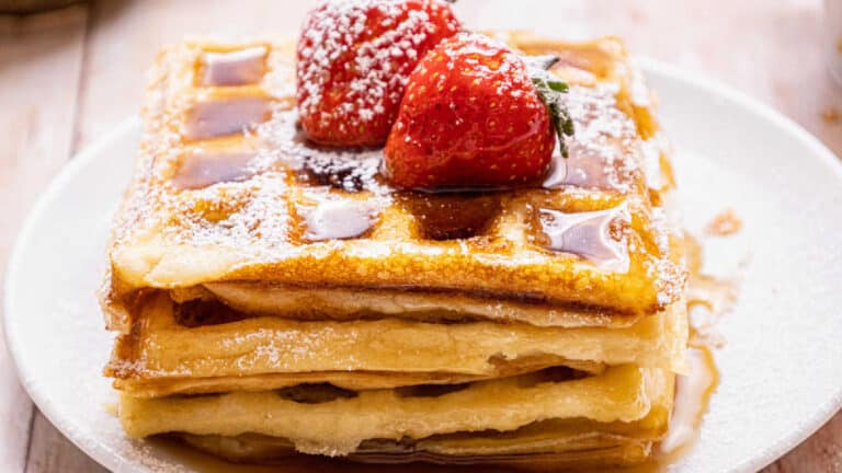 A stack of waffles with maple syrup and strawberries on top.