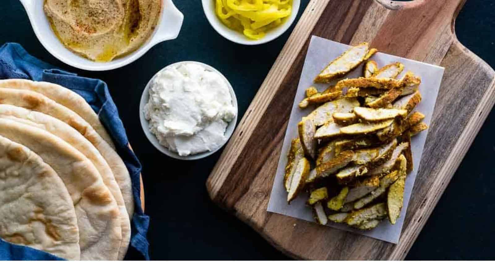 An easy and appetizing combination of pita bread, hummus, and tzatziki sauce showcased on a wooden cutting board.