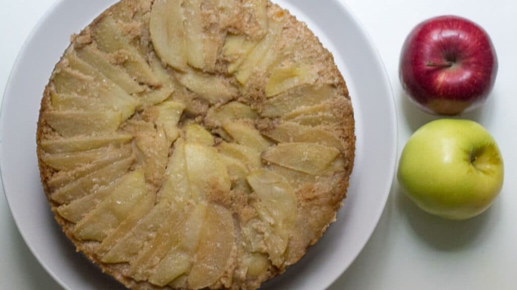 A slice of apple cake on a plate with apples next to it.