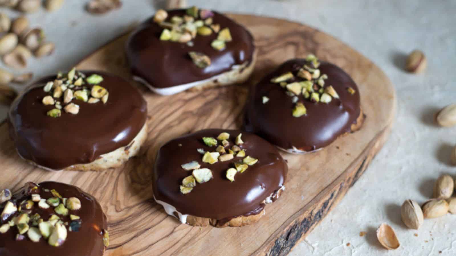 Chocolate pistachio cookies with pistachios on a wooden cutting board.