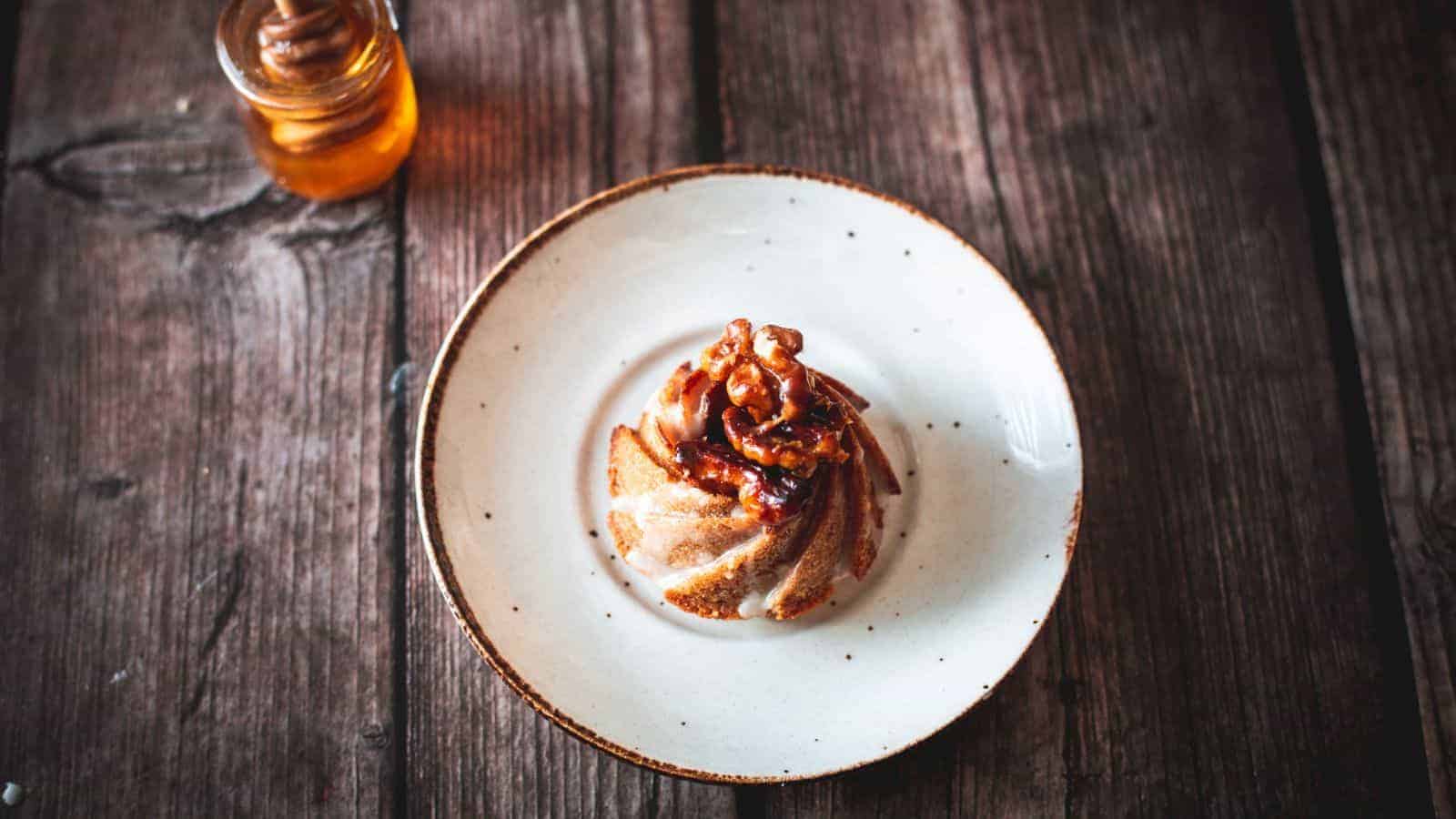 A plate with a pastry on it next to a bottle of honey.