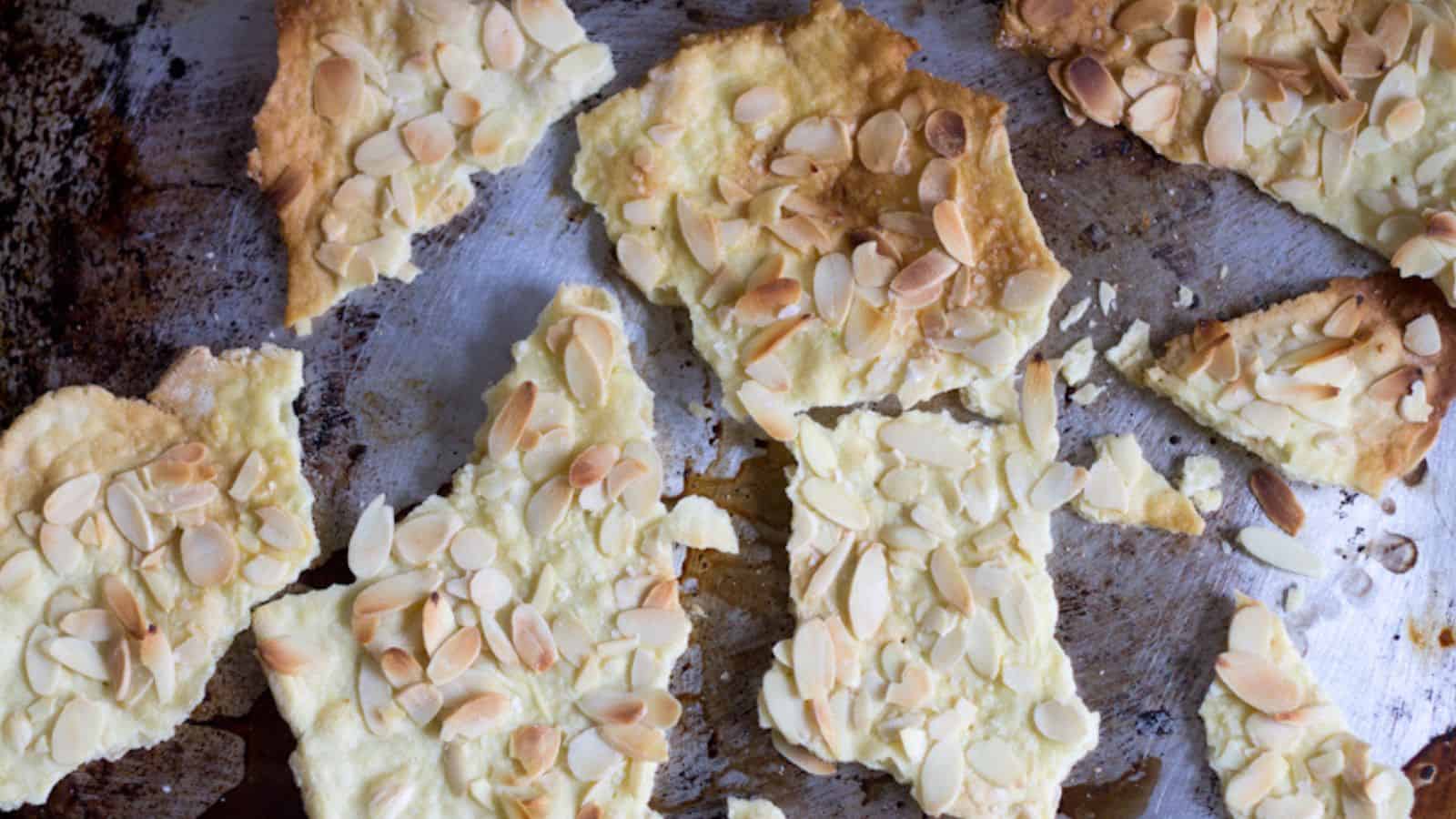 Sliced crackers with almonds on a baking sheet.