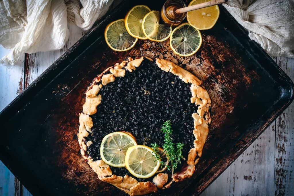 A fruit tart with blueberries and lemon slices on a baking sheet.