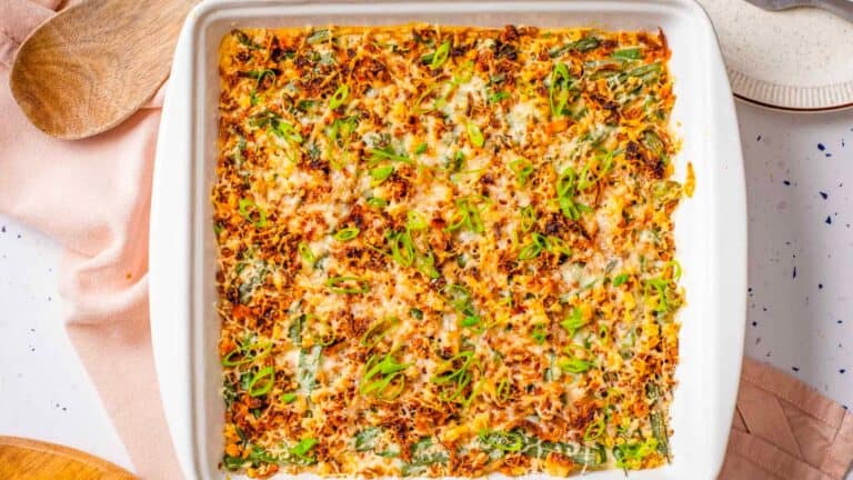 Green bean casserole with cream cheese and scallion topping in white casserole dish.