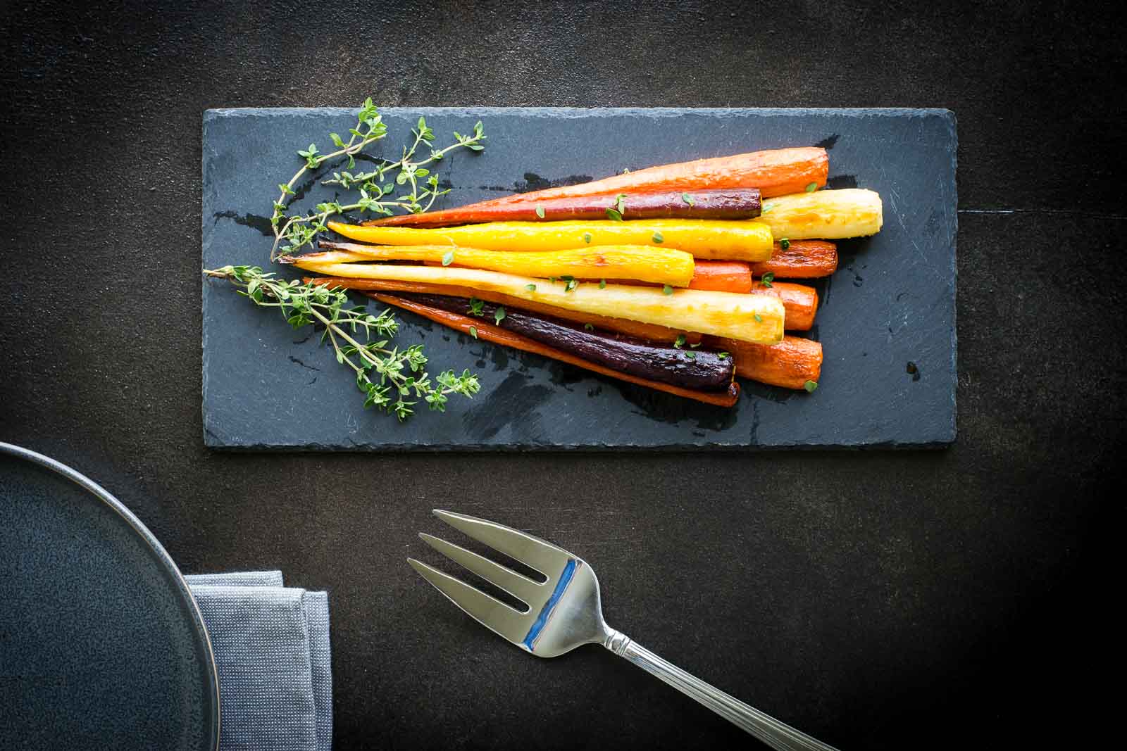 Red, yellow, and orange honey glazed carrots on a slate board.