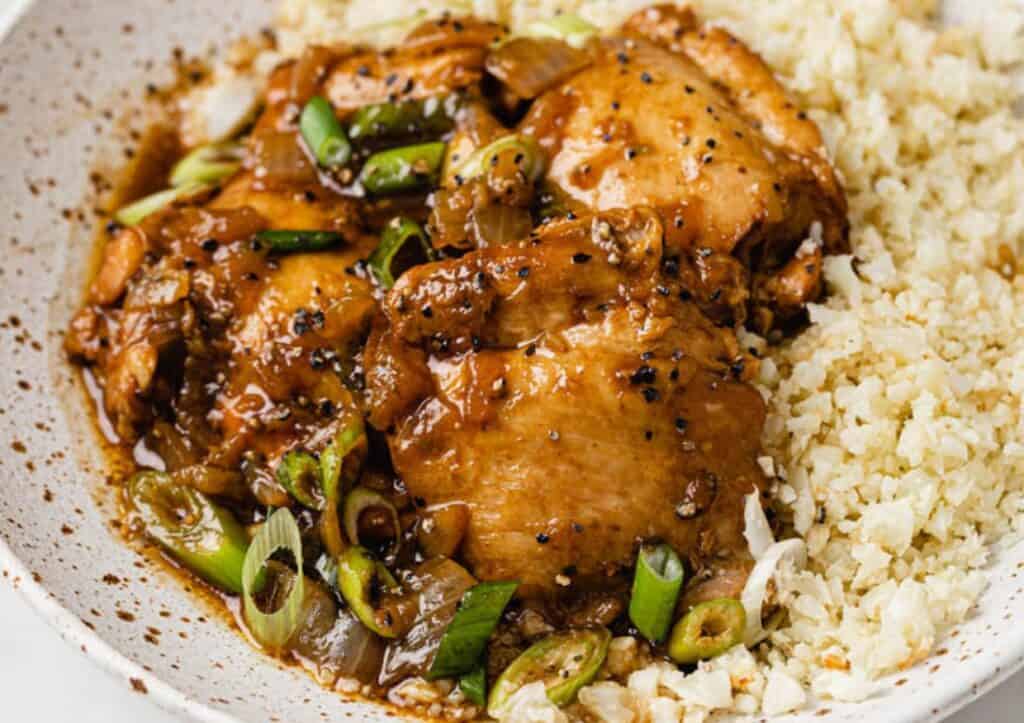 A white bowl with chicken adobo and rice in it.