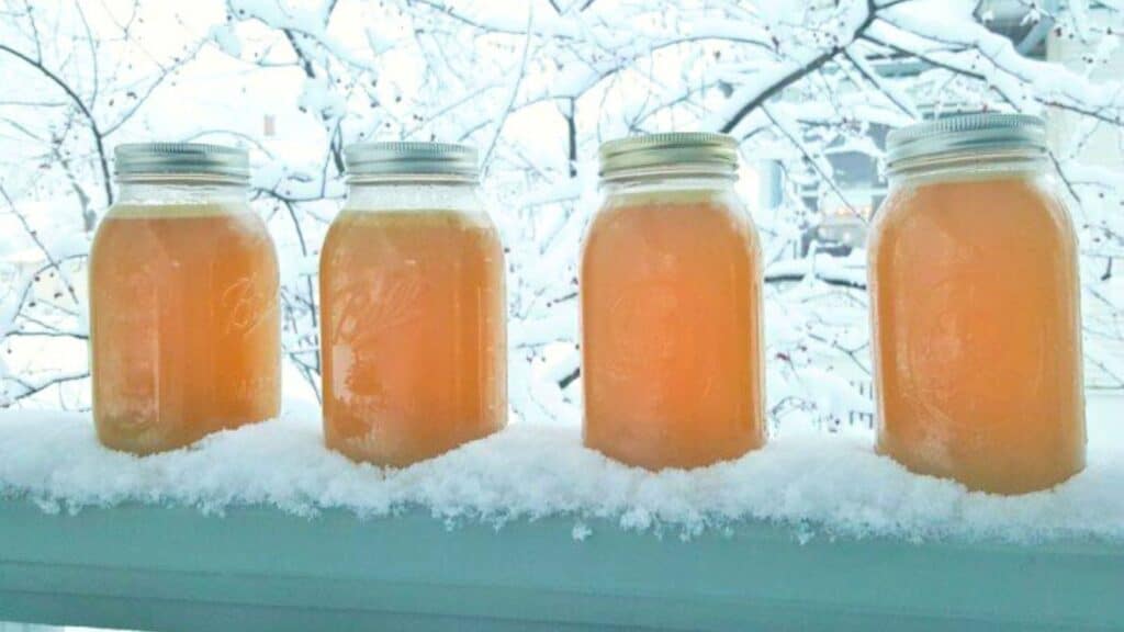Three jars of orange juice sitting on a railing in the snow.