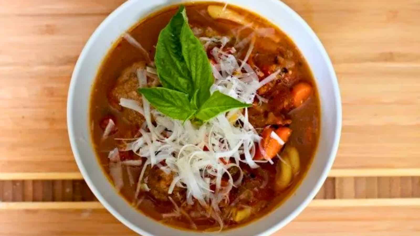 Image shows A bowl of italian meatball soup with a basil leaf on top.