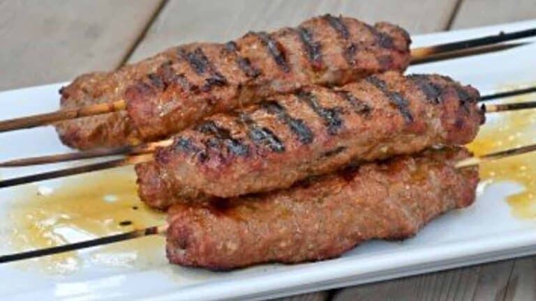 Image shows kefta kebabs stacked on a white tray.