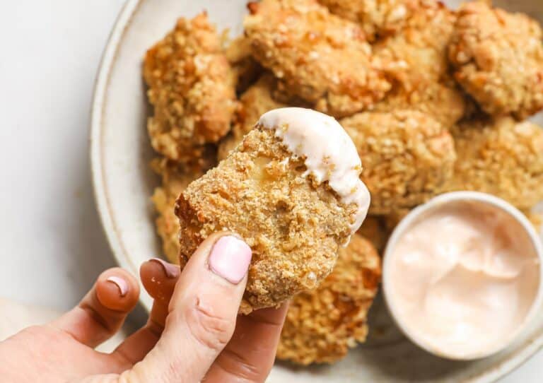 A keto chicken nugget with sauce being held above a plate of nuggets.