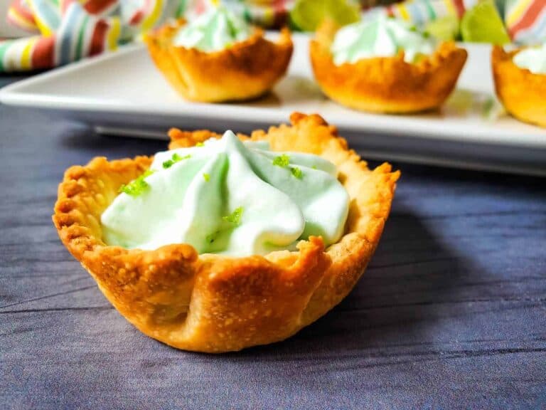 A plate of mini lime tarts with whipped cream and lime wedges.