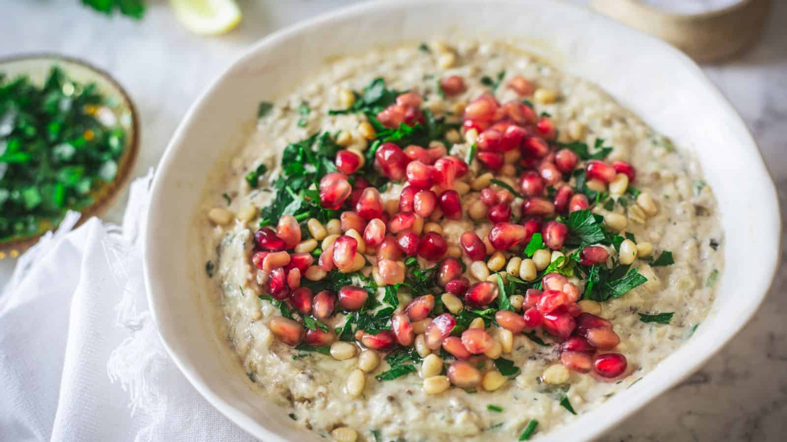 A bowl of hummus with pomegranate and parsley.