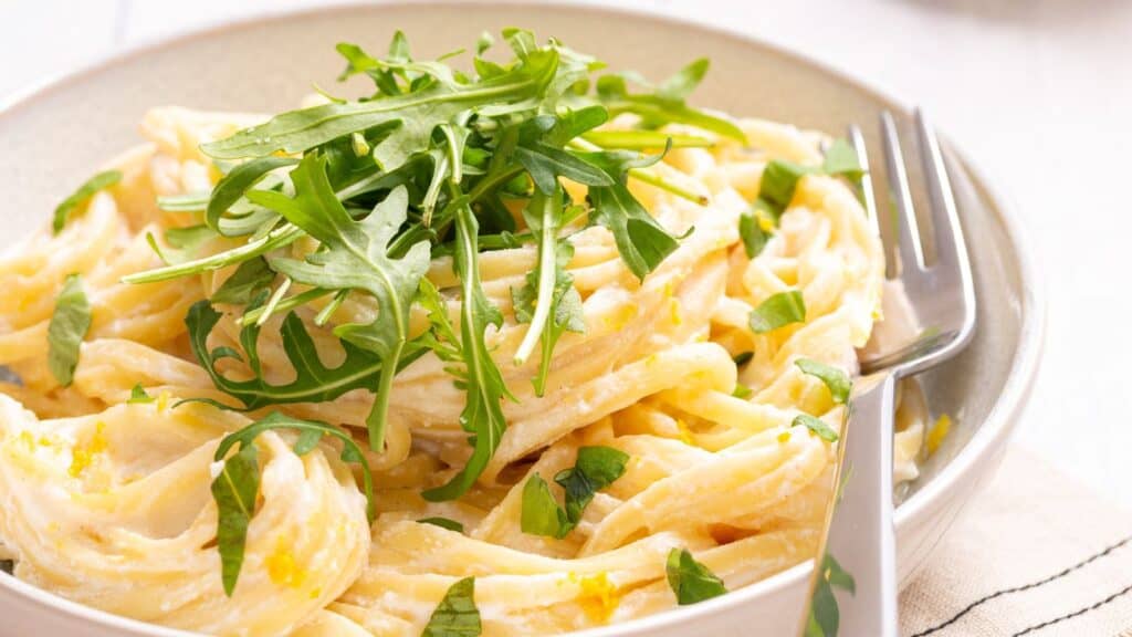 Close up of pasta with cream sauce and arugula on top.