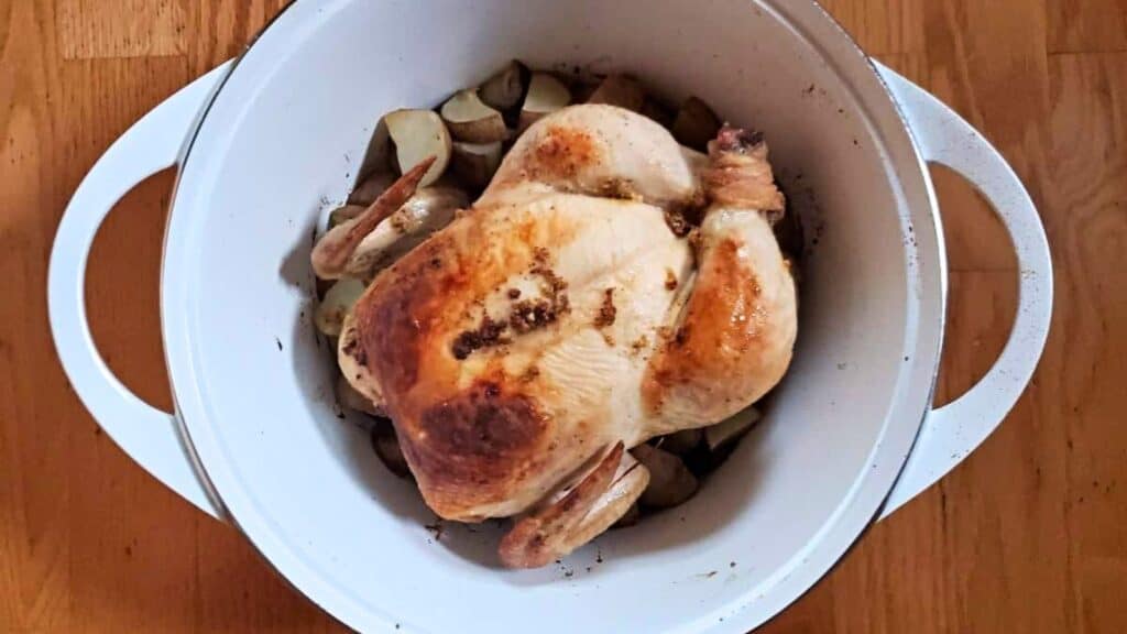 Image shows an overhead shot of lemon roasted chicken in a white Dutch oven.
