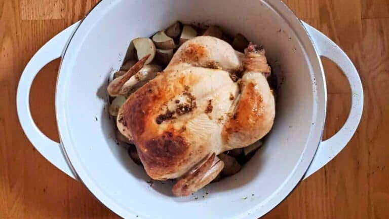 Image shows an overhead shot of lemon roasted chicken in a white Dutch oven.