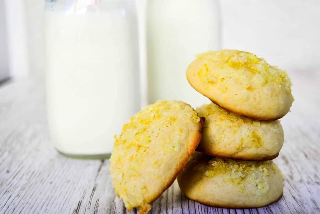 A stack of lemon cookies next to a glass of milk.