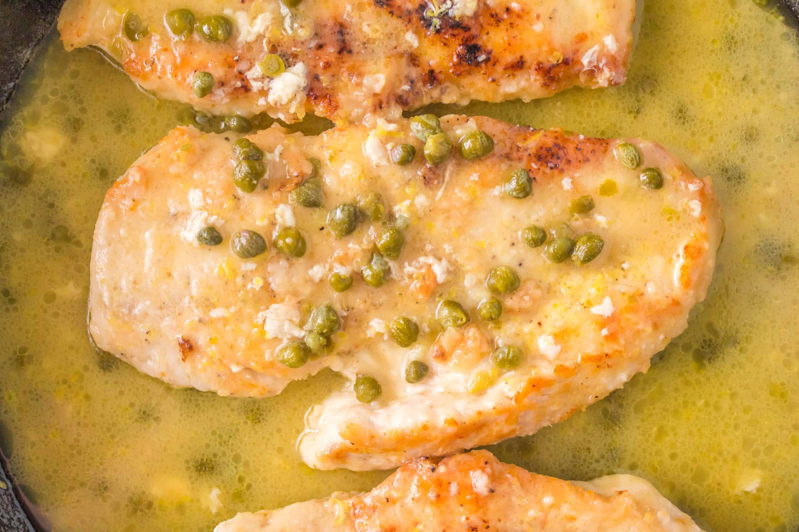 Chicken breasts in a skillet with sauce and peas.