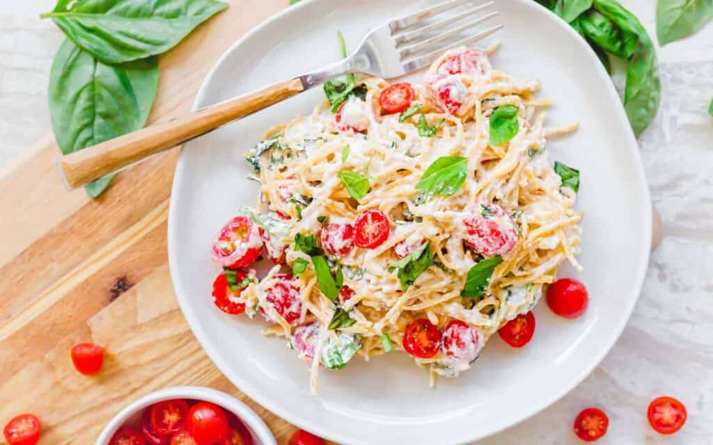 A plate of pasta salad with tomatoes and basil.