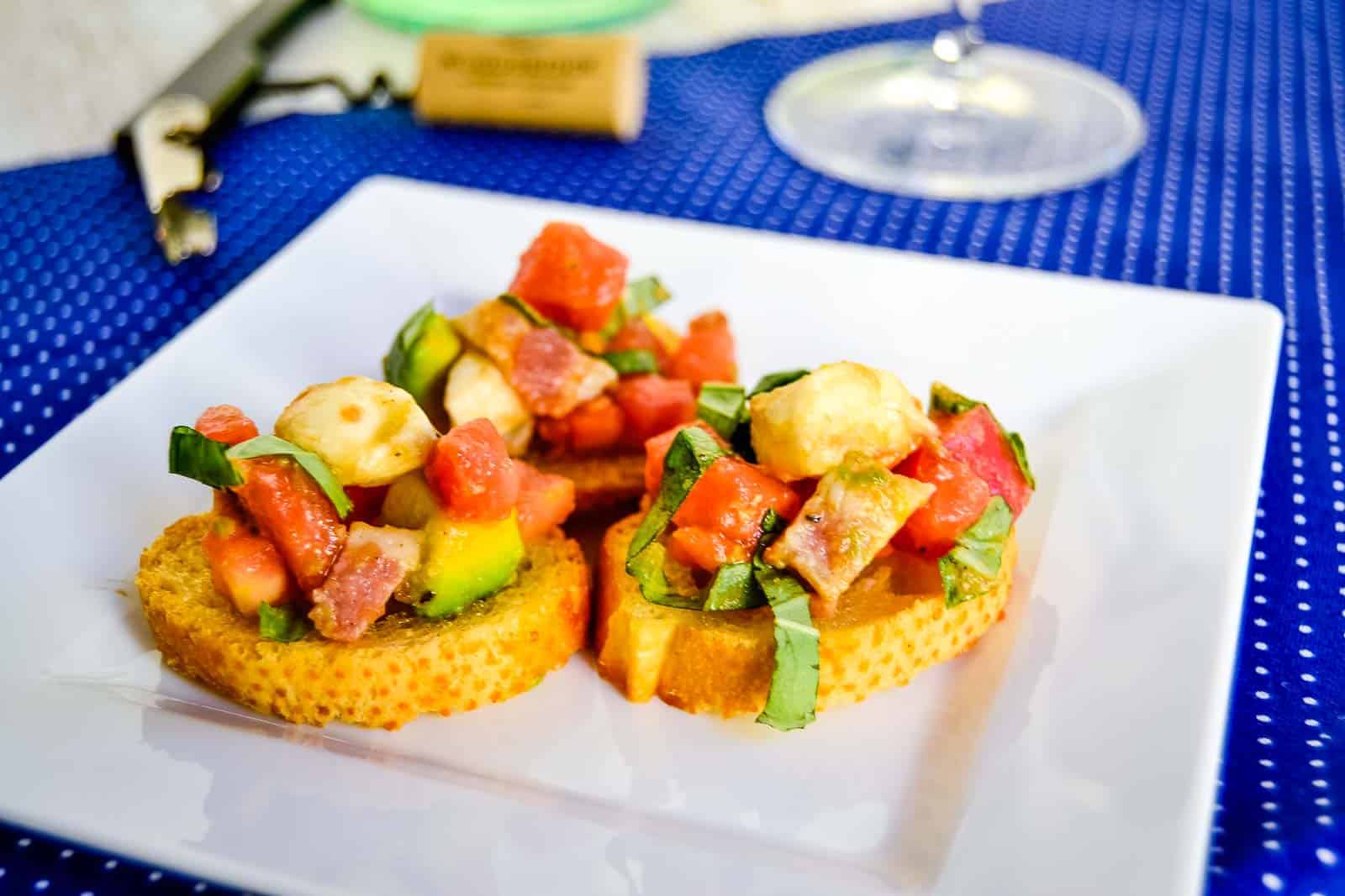 Loaded bruschetta salad on crostini on a white plate.