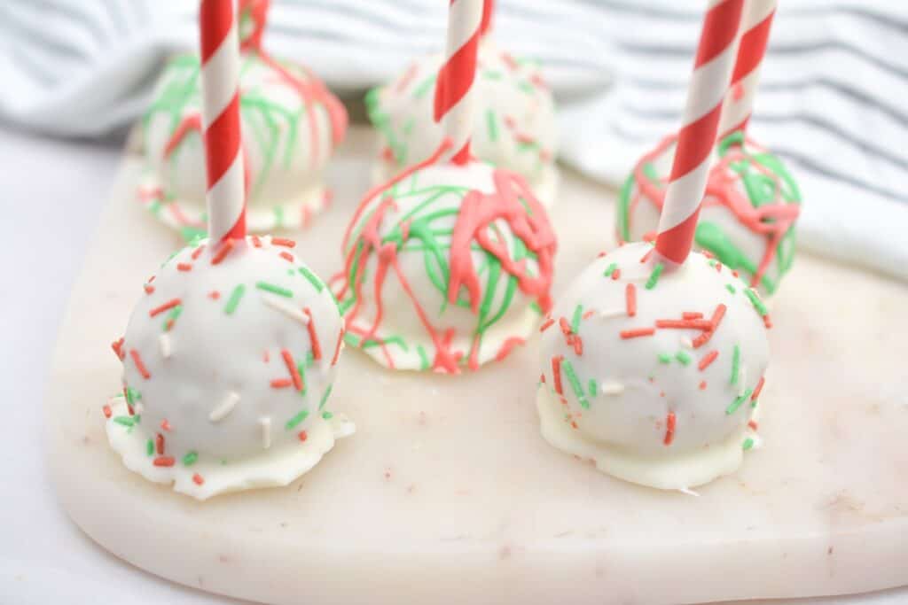 Christmas cake pops with sprinkles on a cutting board.