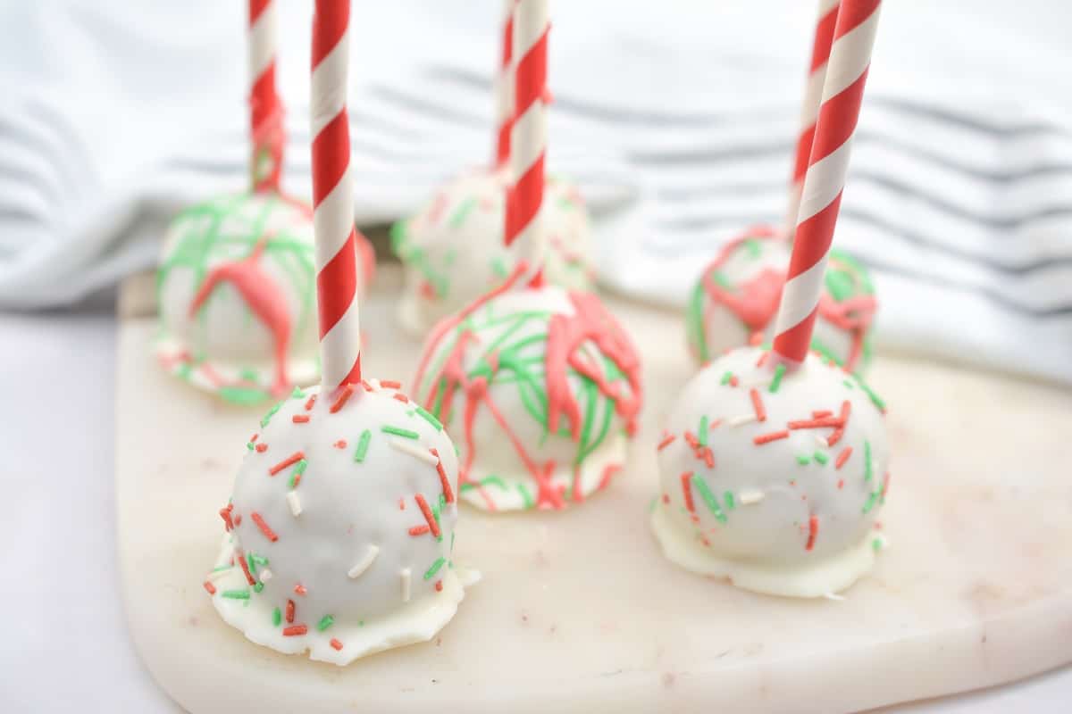 Christmas cake pops with sprinkles and red and white striped straws.