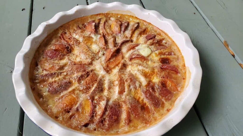 Overhead shot of a whole peach kuchen in a blue ceramic pie pan.