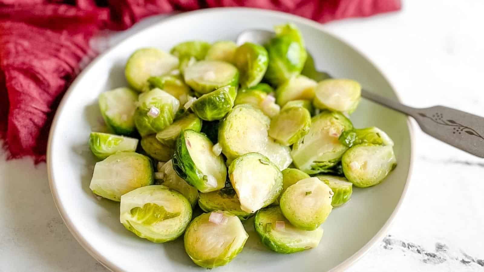 Marinated brussels sprouts are shown on a white plate with a spoon and a dark red linen in the background.