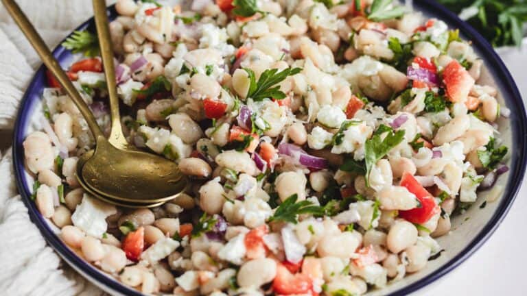 Side view of white bean salad in bowl with tongs.