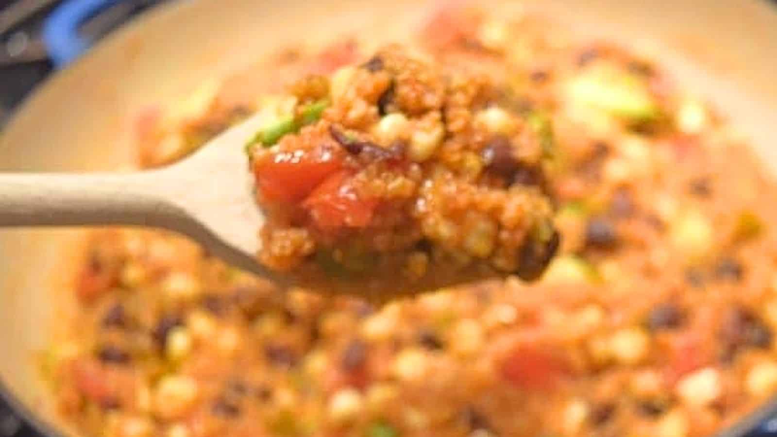 Image shows a wooden spoon holding a scoop of Mexican skillet quinoa with the full pot behind it.